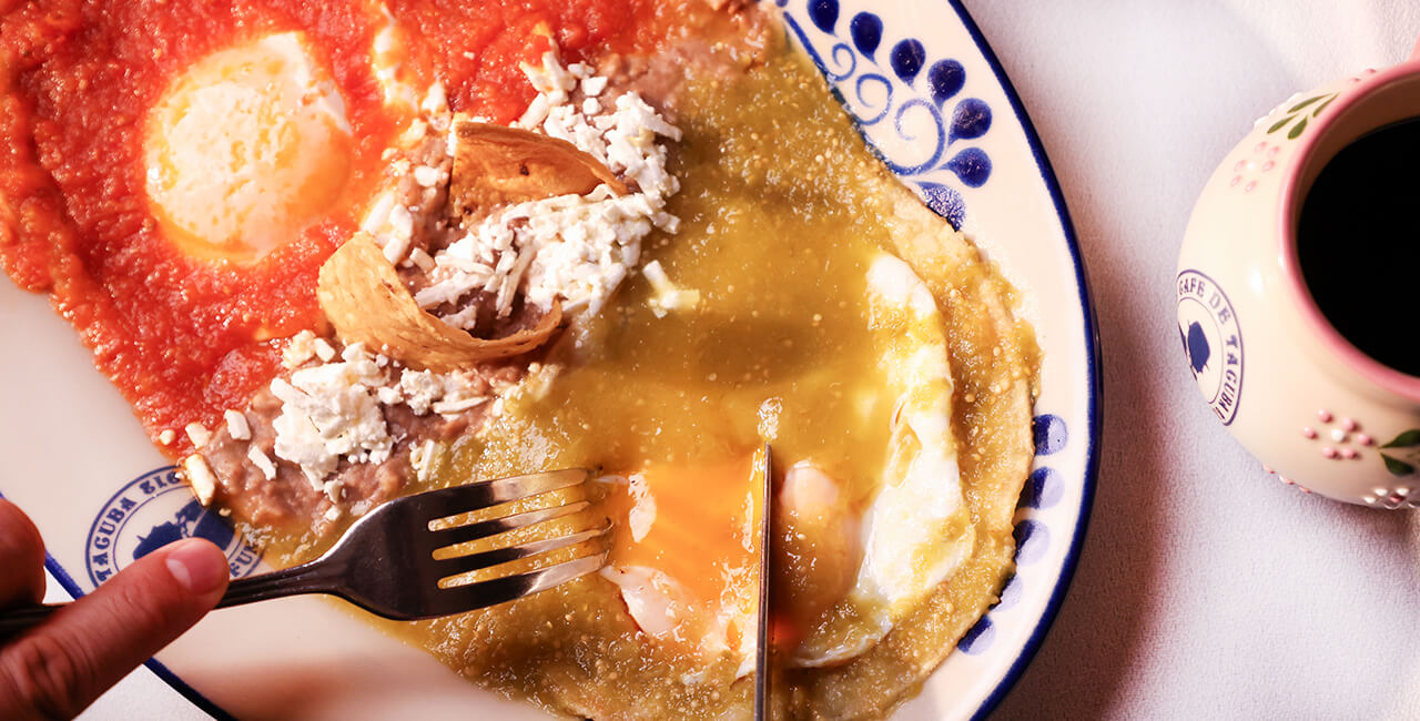 Plato de huevos divorciados con salsa roja y verde, visto desde arriba, con cubiertos iniciando a comer y una taza de caf&eacute; negro en el restaurante Caf&eacute; de Tacuba.