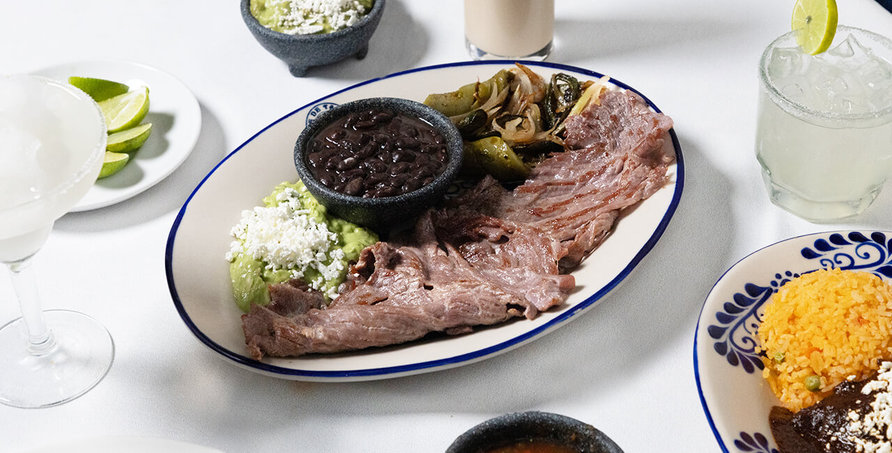 Mesa servida con carne roja asada acompa&ntilde;ada de frijoles, salsas, limones, arroz con mole y bebidas tradicionales en el restaurante Caf&eacute; de Tacuba.